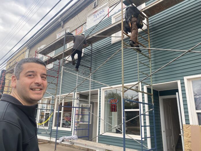 Diyaa-beaut-1 med Pizza L'Amore owner Diyaa Salaam in front of his Main St. building, where workers are installing new siding under the Town of Oxford Beautification Program